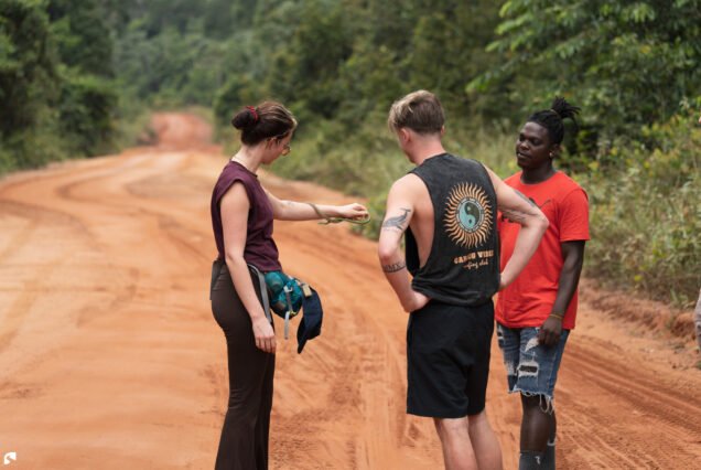 Tour guide Juri in a red shirt interacting with guests along a laterite road during a rainforest expedition in Suriname.