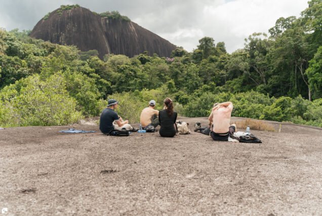 Four hikers resting on a granite outcrop overlooking Voltzberg and the tropical rainforest in Suriname.